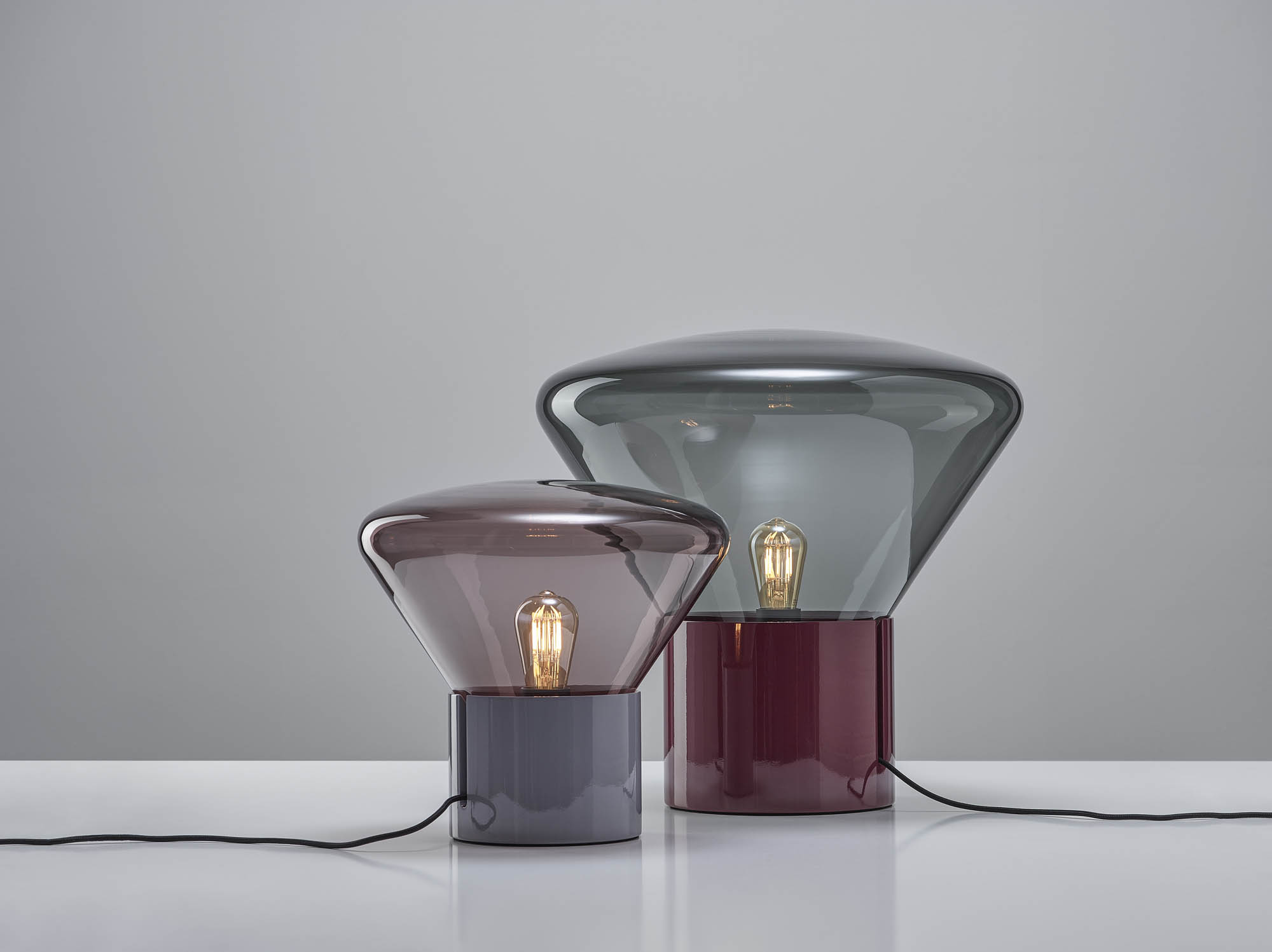 Brokis Muffins table lamps with smoky and blue-grey domes, crystal bases, and glowing bulbs on a white surface.