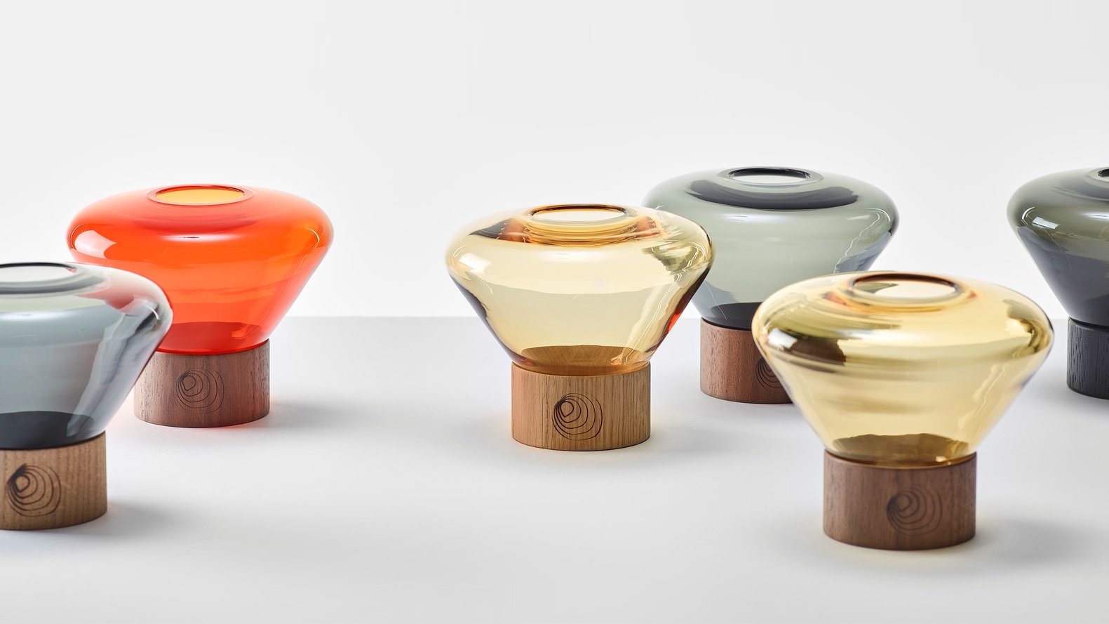 Five Brokis Muffins Candleholders in rich orange, amber, and grey rest on smooth wood bases, elegantly arranged,