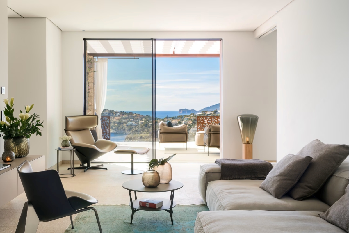 A sun-drenched living room with Brokis Muffins Wood 04 opens to a balcony overlooking a breathtaking coastal panorama.