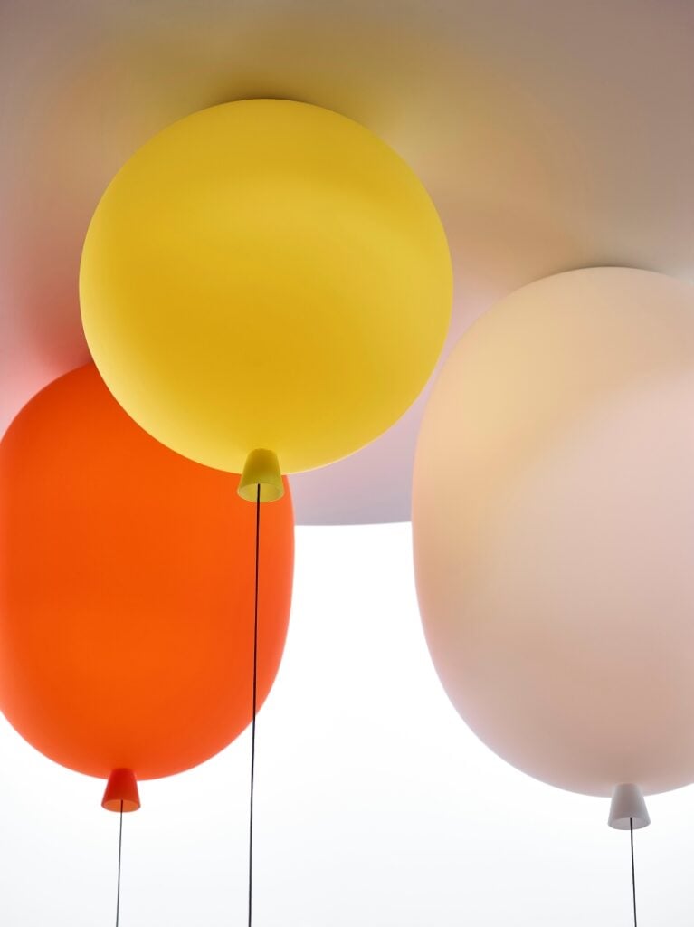 Three Brokis Memory ceiling lights - yellow, red-orange, and pink glass shades - with black strings trailing below.