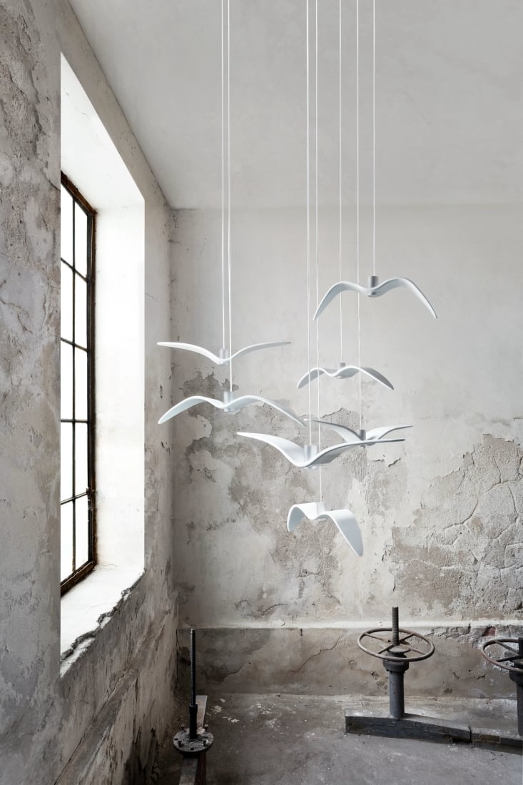 Brokis Night Birds Pendants glide above a sun-drenched, weathered room adorned with cracked plaster and vintage steel.