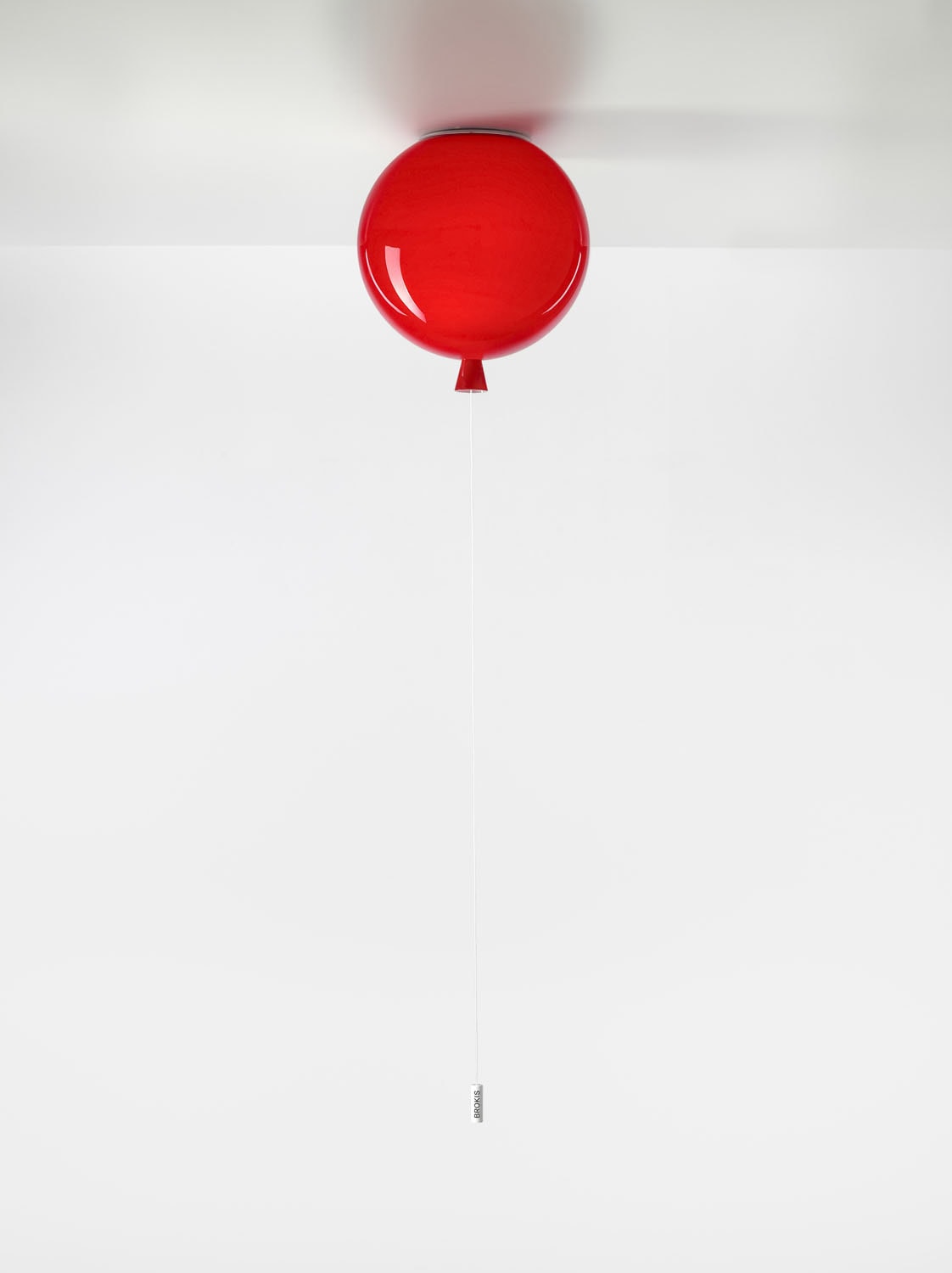 Brokis Memory Ceiling 250 red balloon with white cord hangs against a backdrop, anchored by its gleaming glass weight.