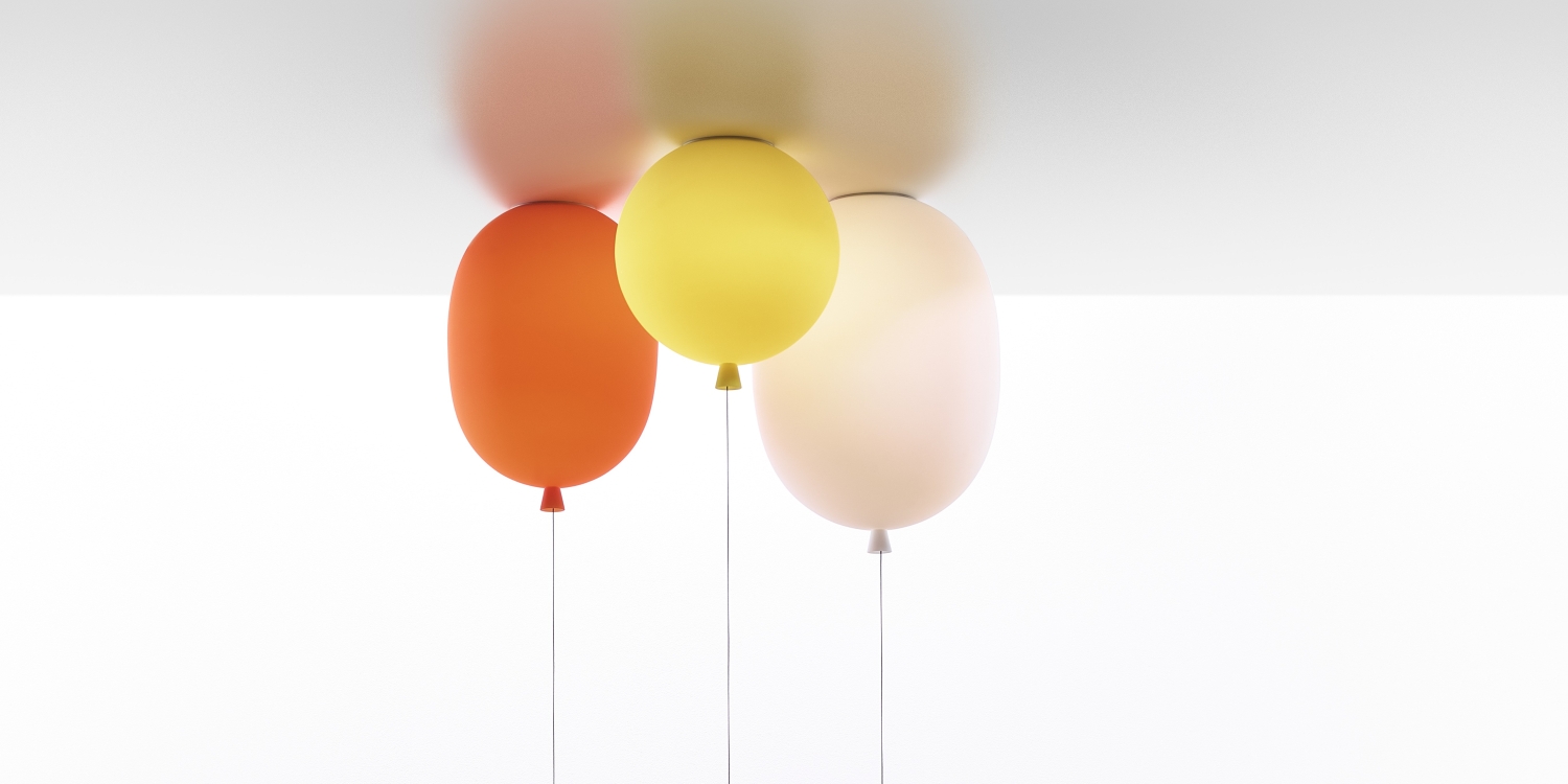Three Brokis Memory Oval lights in orange, yellow, and light pink float upside down near a white ceiling on slender strings.