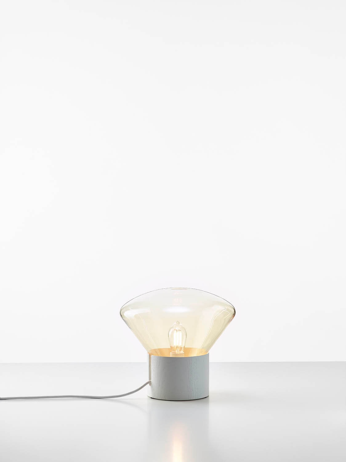 Brokis Muffins Mini Wood 06 lamp, with a sculptural glass shade and sleek base, emits a luxurious warm glow.