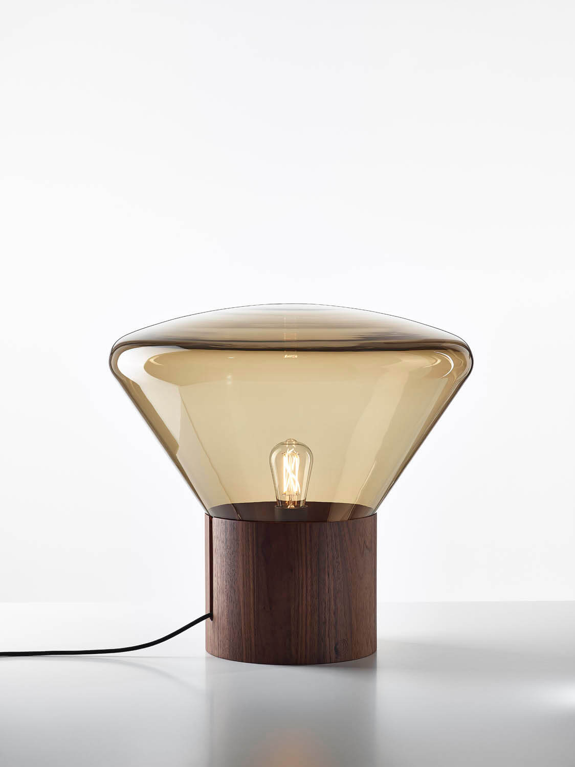 Brokis Muffins Wood 02 table lamp with amber handblown glass, sculptural wooden base, and exposed bulb casting a warm glow.