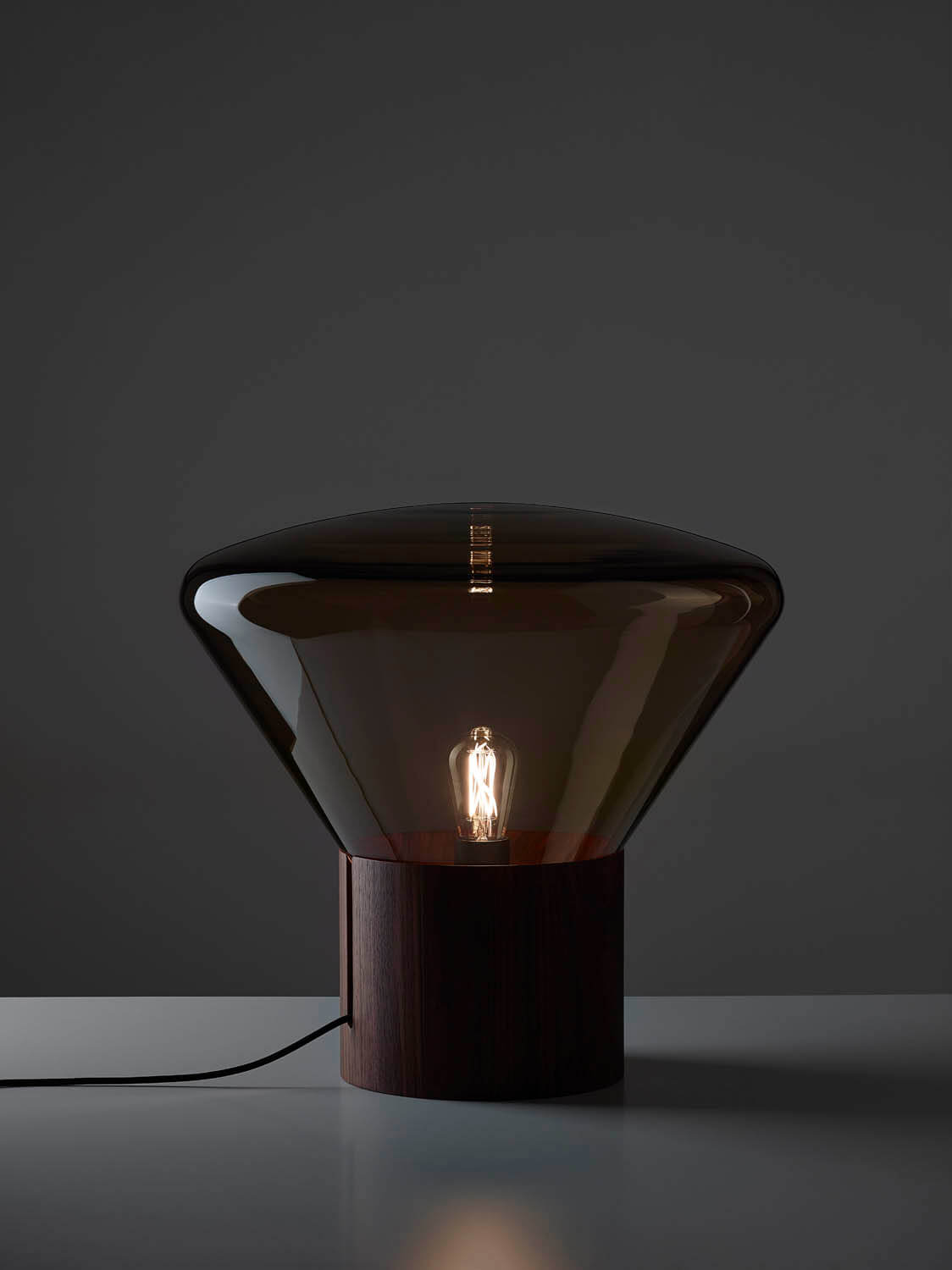 Brokis Muffins Wood 02 lamp boasts a sculptural, handblown glass shade and dark wood base, glowing with elegance.
