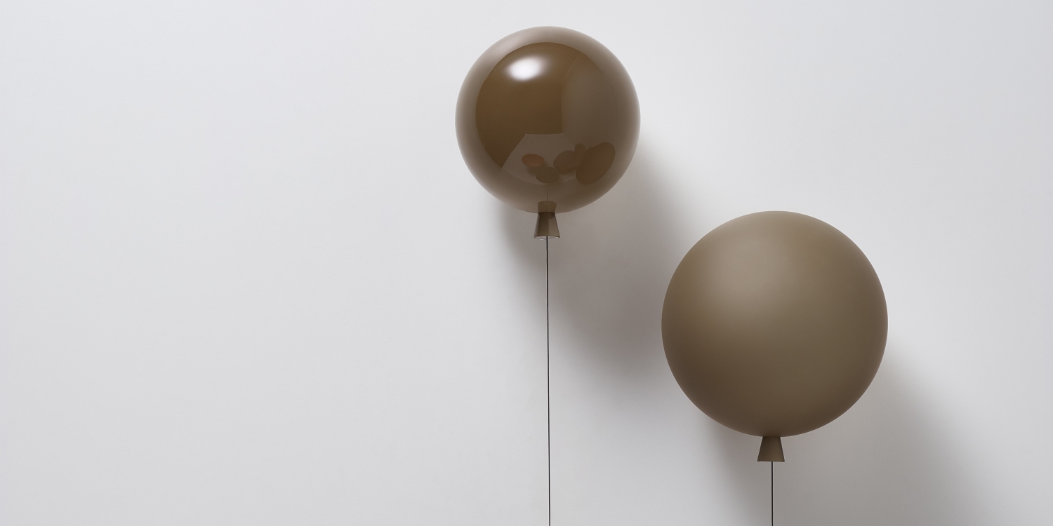 Two Brokis Memory Wall lights float elegantly against a white wall, one glossy, the other matt, each anchored by a string.