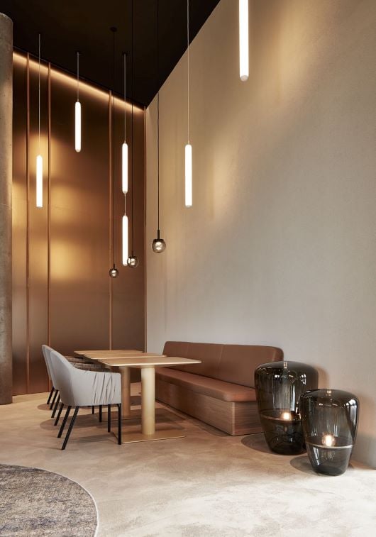 A modern dining area with a light wood table, brown leather bench, grey chairs, and Brokis Puro pendant lights.