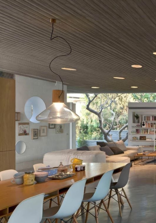 A modern dining space with Brokis Muffins Wood 03B Pendant, white chairs, in a concrete interior.