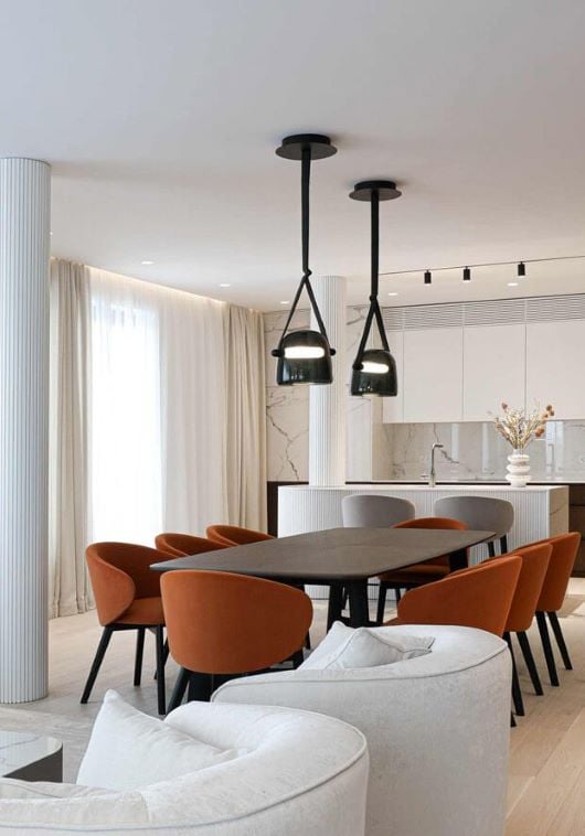 Sophisticated dining area with dark table, six burnt orange chairs, and Brokis Mona Median Pendants.
