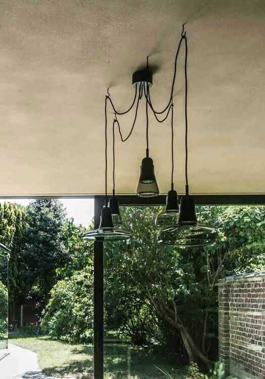 Brokis Shadows Set Free with transparent glass and elegant black cords glow softly above, framed by windows to lush gardens.