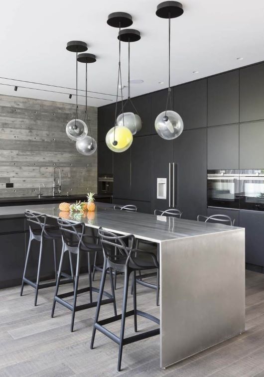 Matte black cabinetry and a stainless steel island anchor the space, crowned by Brokis Capsula Single Pendants above.