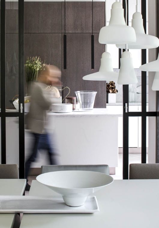 A person rushes through a sleek kitchen with dark wood cupboards, white island, Shadows pendants, and elegant decor.