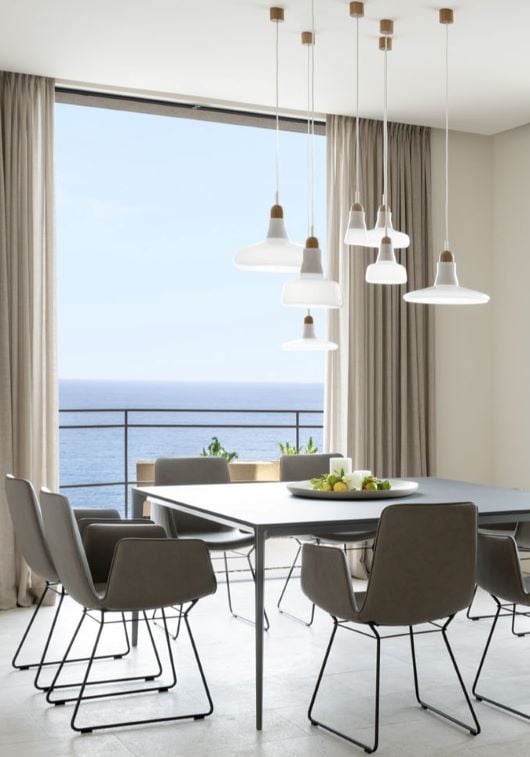 A modern dining room with sea view, black table, grey chairs, Brokis Shadows, beige curtains, and a bowl of lemons.