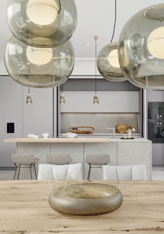An airy modern kitchen with Brokis Big One Large Pendants, marble island, light grey cabinetry, and elegant minimal decor.