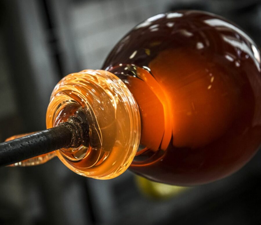 Brokis molten glass being shaped on a metal blowpipe, swirling and glowing from intense heat.