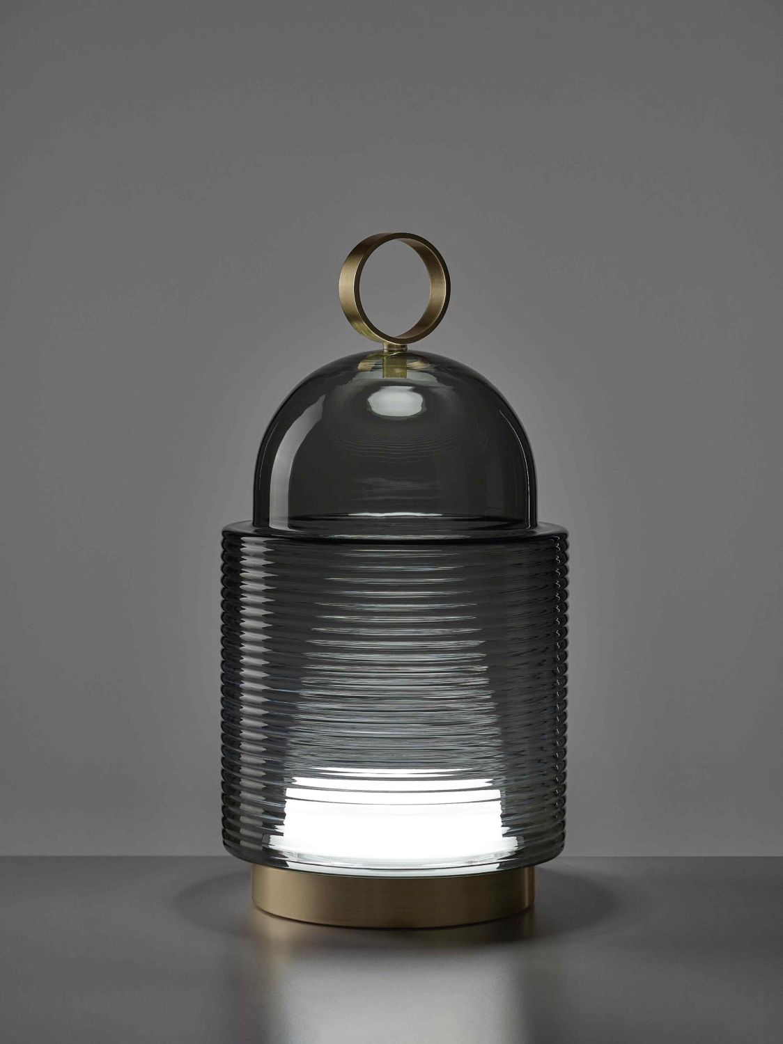 Brokis Dome Nomad Large lamp showcases a sculptural ribbed glass base, glowing light, and elegant gold handle atop its dome.