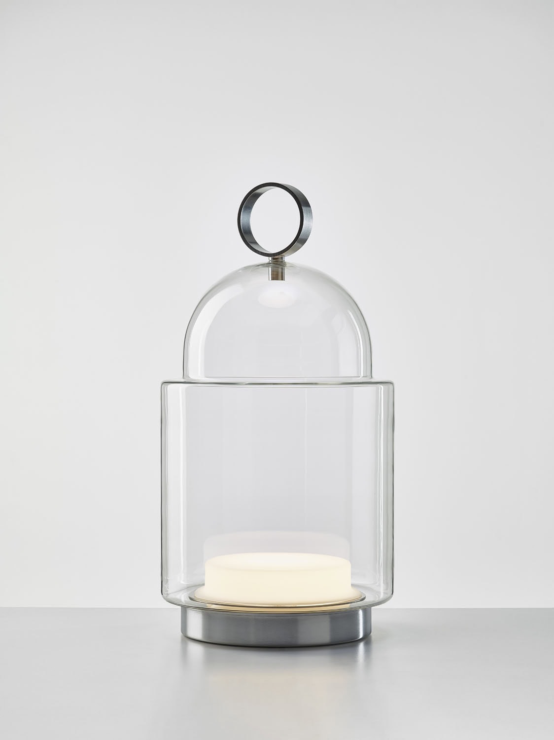 Brokis Dome Nomad Large is a sculptural handblown glass lantern, softly glowing atop a sleek surface with a metal handle.