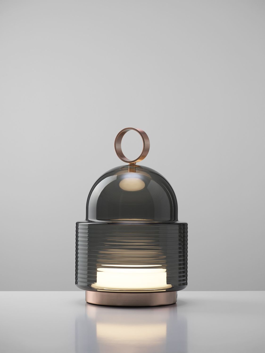 Brokis Dome Nomad Small lamp features sculptural glass and copper, softly glowing on a white surface.