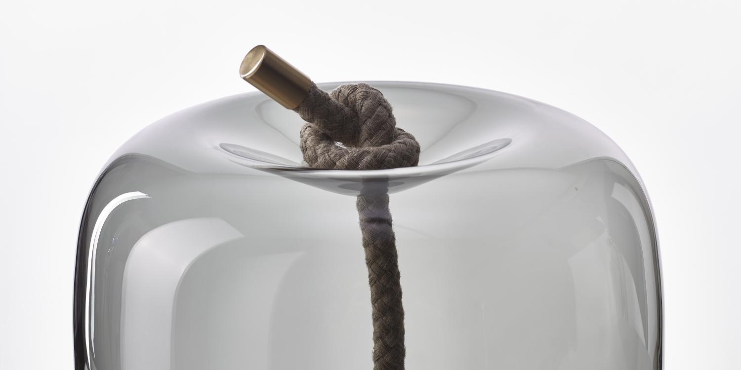 A Brokis Knot Cilindro Table pairs a thick knotted rope and brass detail with handblown glass on a white backdrop.