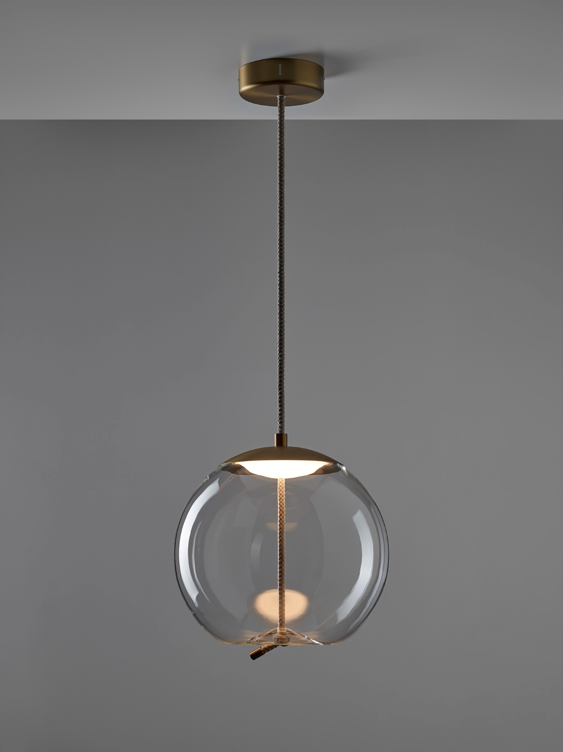 Brokis Knot Sfera Pendant showcases a handblown glass globe, brass accents, and rope, set against a grey backdrop.