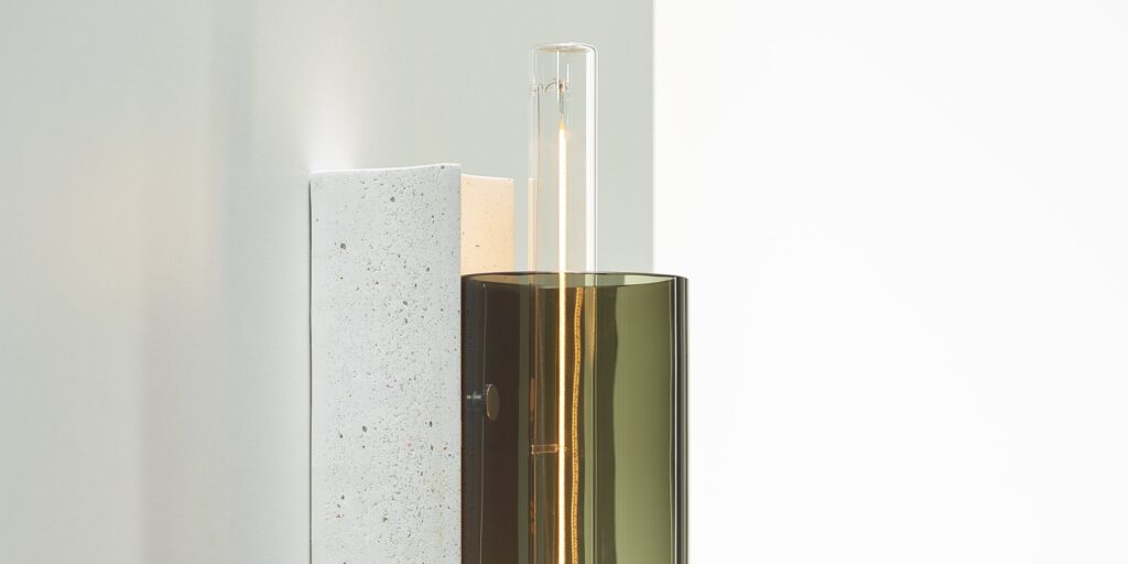 Brokis Overlay Wall M features handblown olive green glass and sculptural concrete, casting a refined ambient glow.