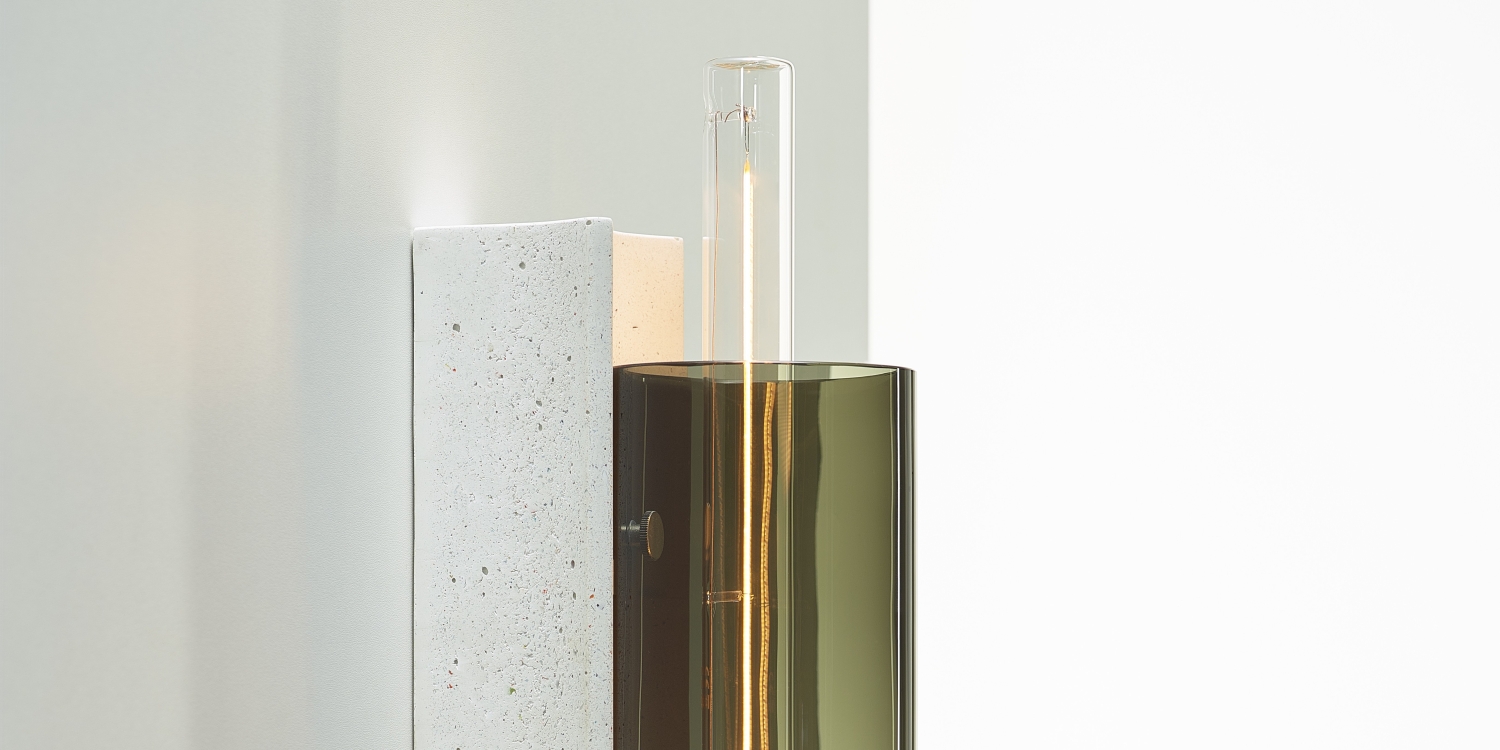 Brokis Overlay Wall M features handblown olive green glass and sculptural concrete, casting a refined ambient glow.