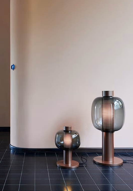 Brokis Bonbori lamps with sculptural copper bases and grey glass glow warmly on a glossy black tiled floor.