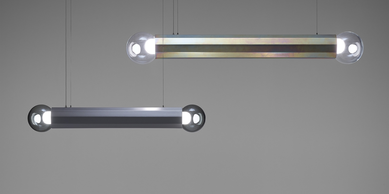 Brokis Prisma Chandeliers in zinc and silver hang elegantly, their sculptural forms aglow against a grey backdrop.