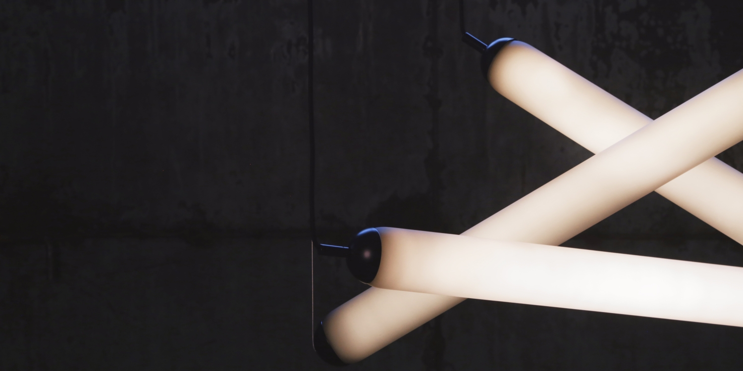 Brokis Puro Eclectric Rectangular Set light tubes with dark caps form a glowing, sculptural pattern on a dark concrete wall.