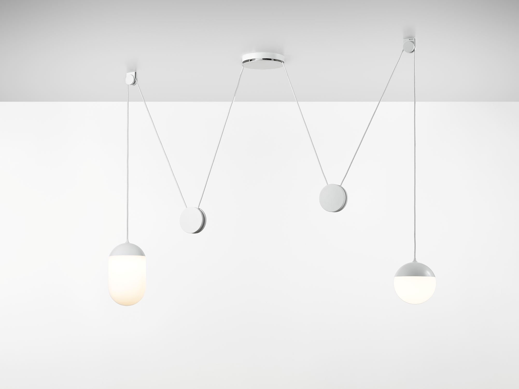 Brokis Planets 2 Set showcases sculptural hand-blown ceiling lights - one elongated aglow, one round unlit - on white cords.