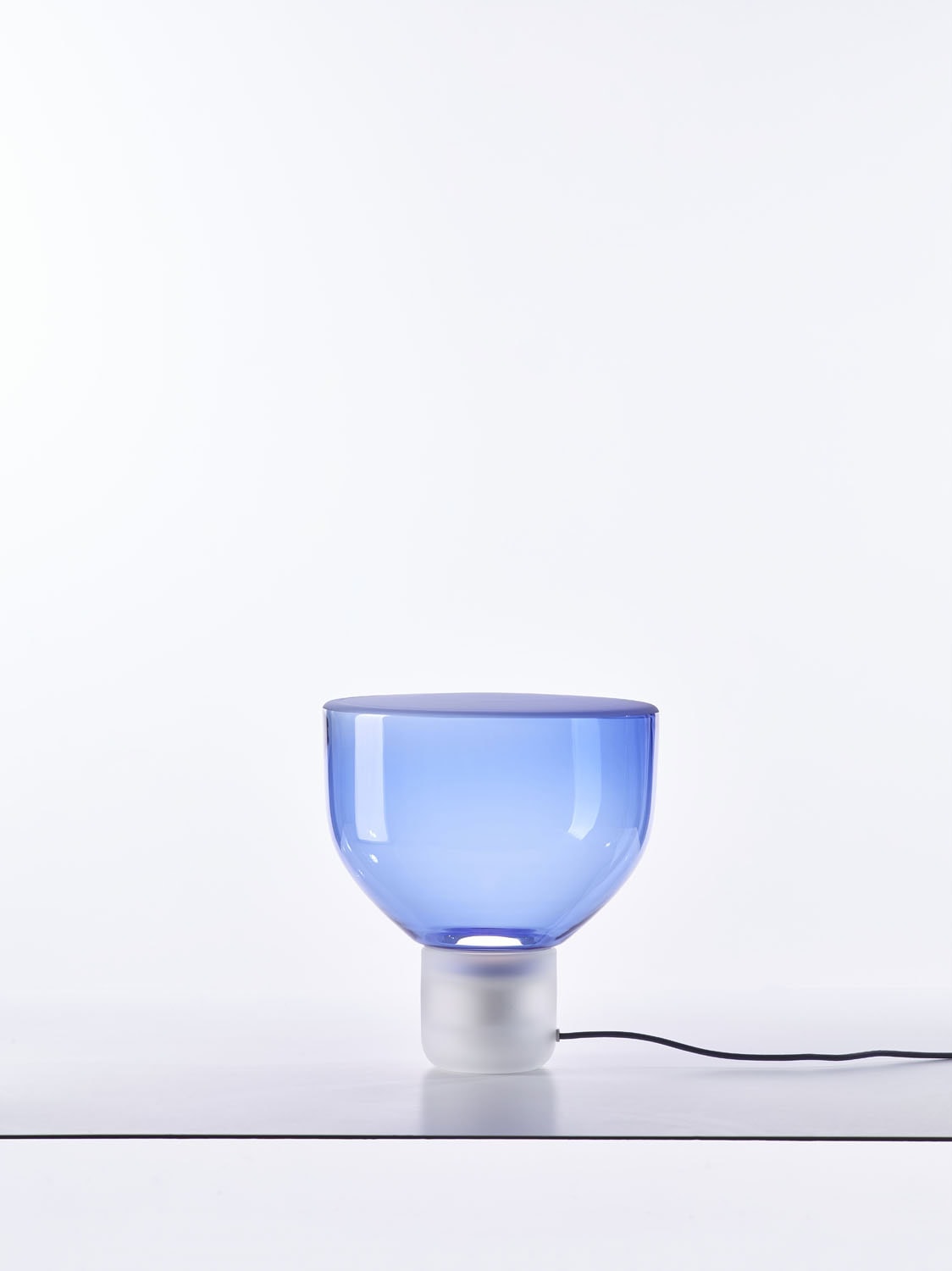 Brokis Lightline S Table lamp, handblown blue glass and white base, rests elegantly on a sleek white surface.