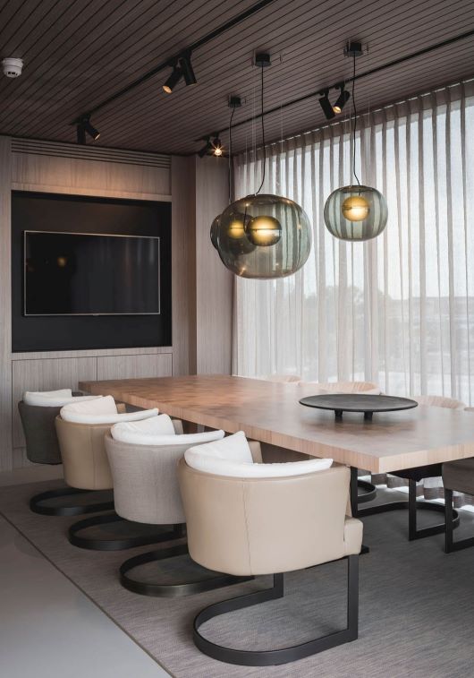 Six beige chairs surround a light wood table beneath Brokis Big One pendants; sheer curtains add sophistication.