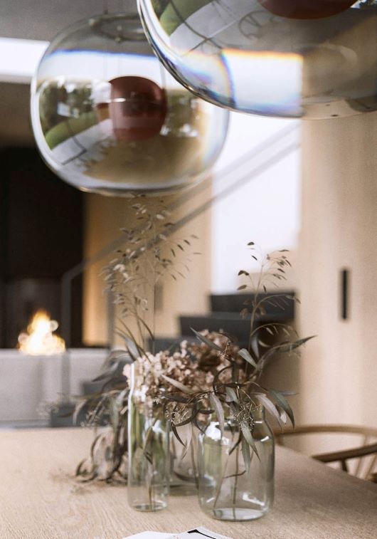 Elegant dining table with glass vases of dried florals, beneath two Brokis Big One Large pendant lights; fireplace alight.