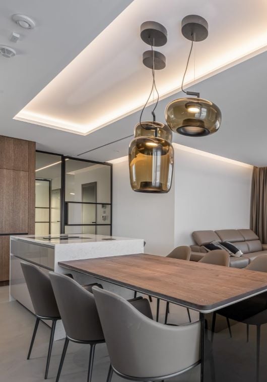 A chic dining area with taupe chairs, wooden table, Brokis Double pendant lighting, marble island, and minimalist accents.