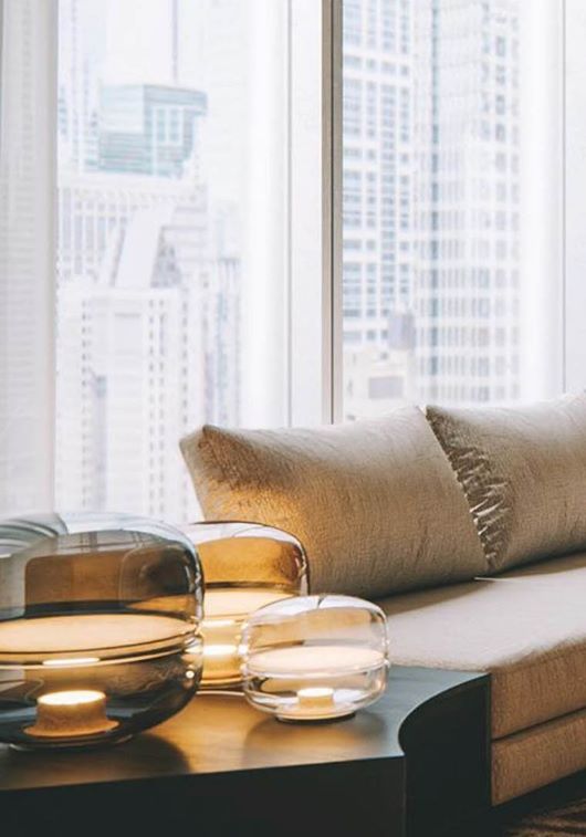 A modern living room features a beige sofa, with sculptural Brokis Macaron lamps glowing by tall windows.