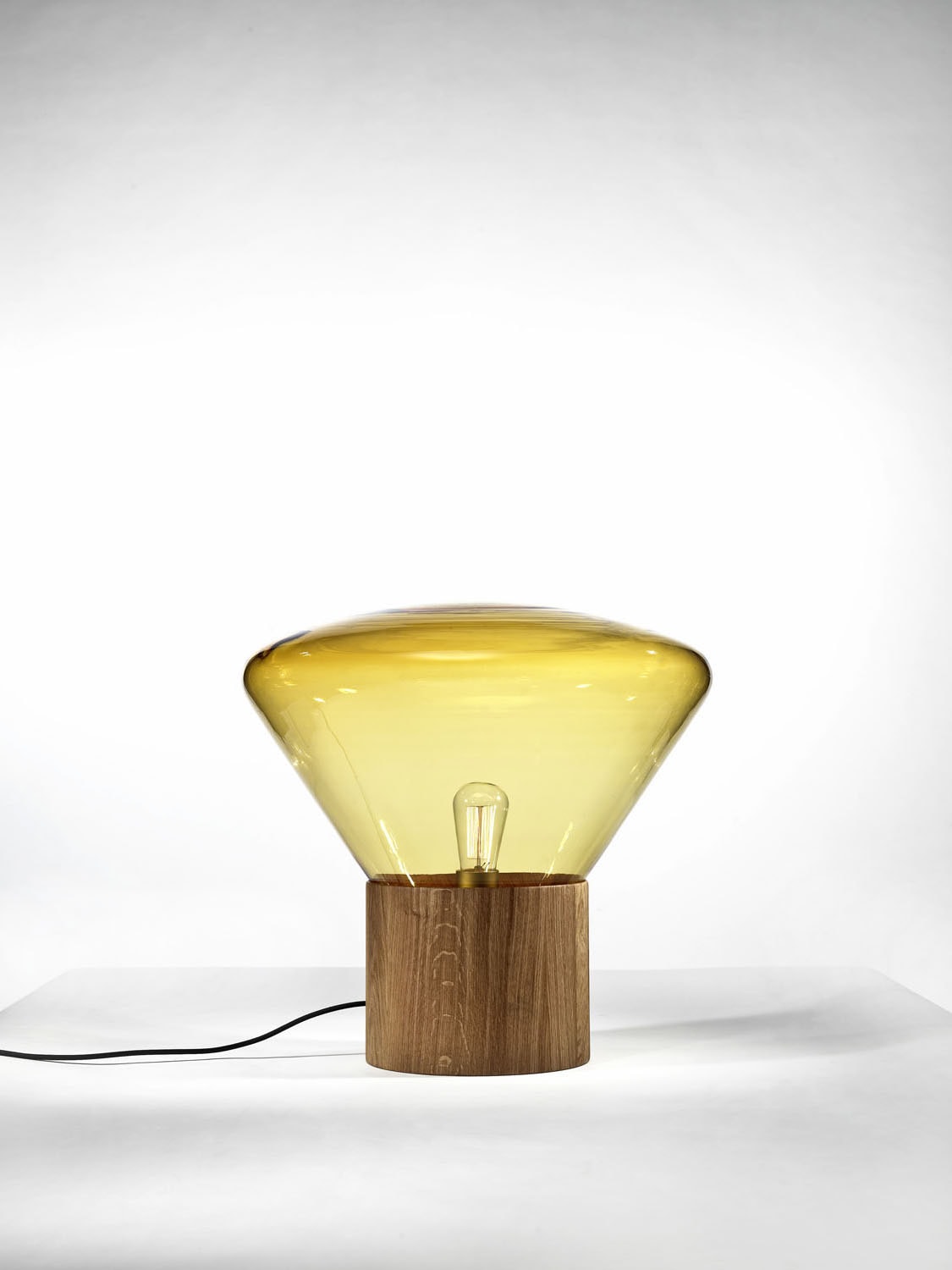 Brokis Muffins Wood 01 lamp with sculptural handblown amber glass shade and wood base, set against a white background.