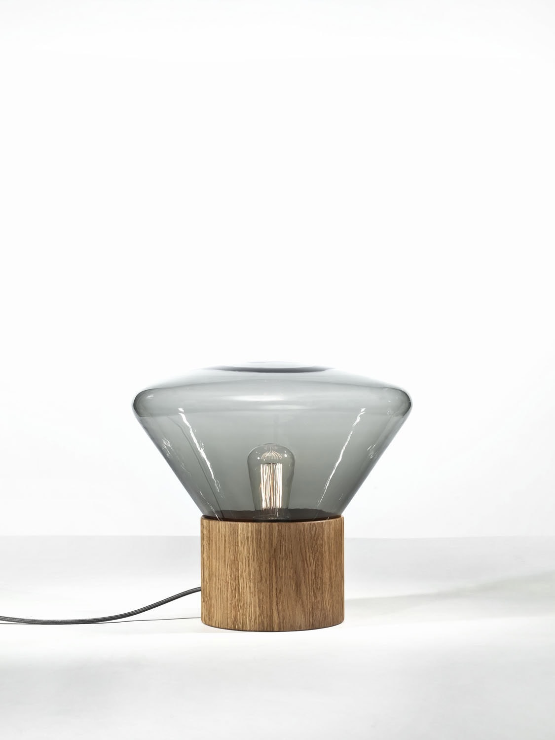 Brokis Muffins Wood 01 lamp pairs a sculpted wood base with a handblown grey glass shade, revealing the bulb within.