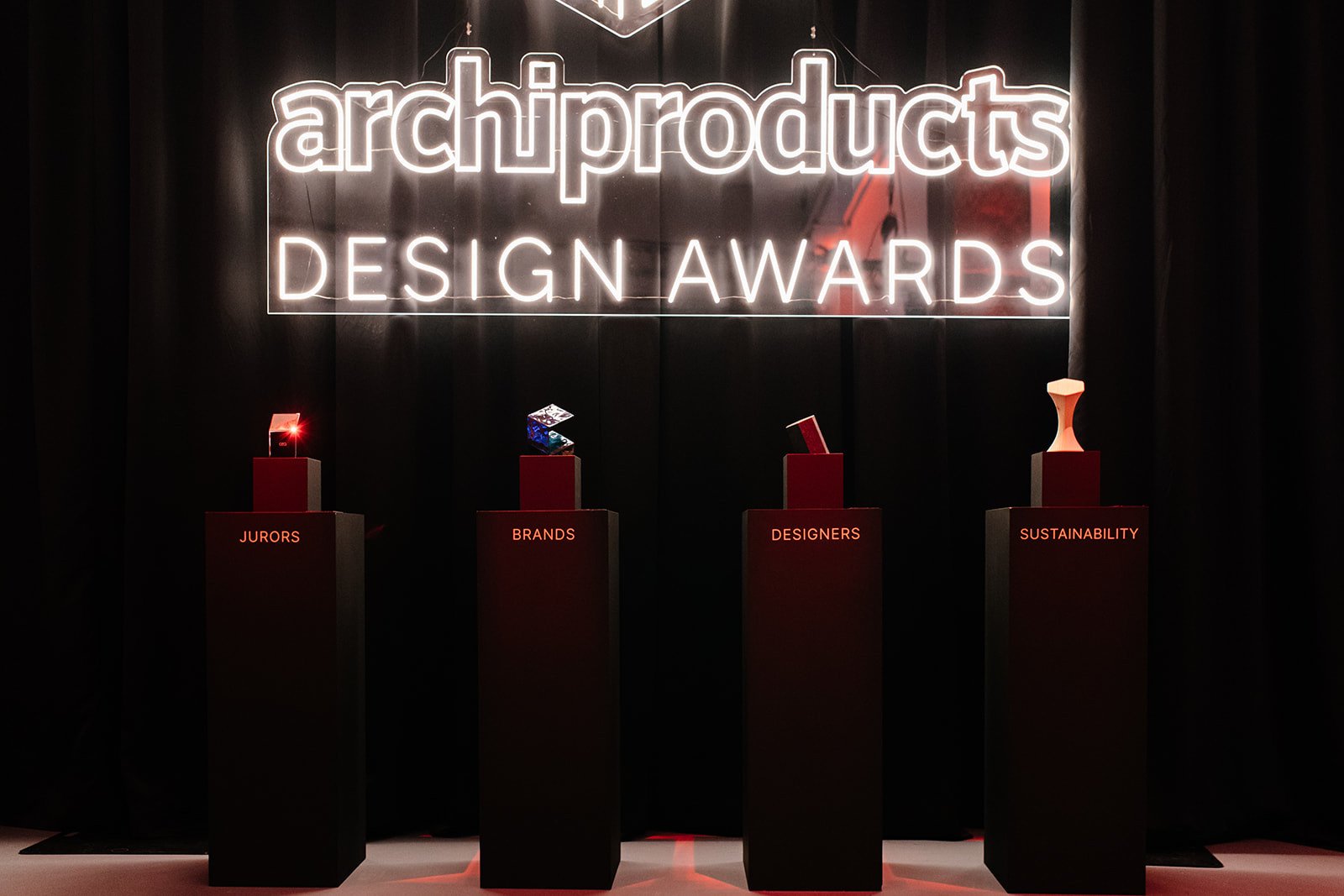 Four black podiums labelled JURORS, BRANDS, DESIGNERS, SUSTAINABILITY beneath a glowing award sign and elegant trophies.