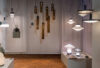 A lighting showroom features sculptural, hand-blown Brokis pendant, wall, and table lamps aglow on sleek white plinths.