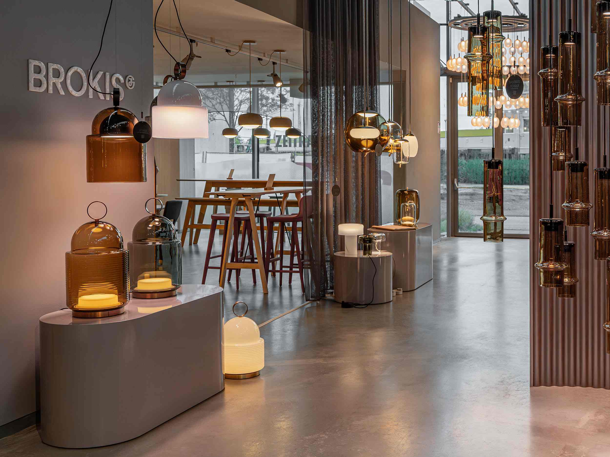 A showroom showcases sculptural Brokis handblown glass and metal lamps, luxe seating, and sunlit polished concrete floors.