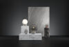 Brokis Sfera Portable lamps in varied sizes glow atop marble pedestals, set before a towering grey stone slab.