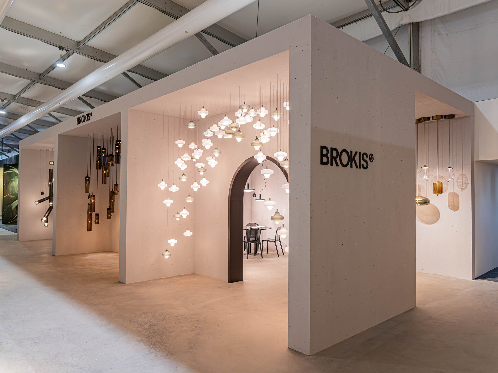 A modern showroom showcases Brokis glass pendant lights, illuminating a minimalist entrance with sleek furnishings.