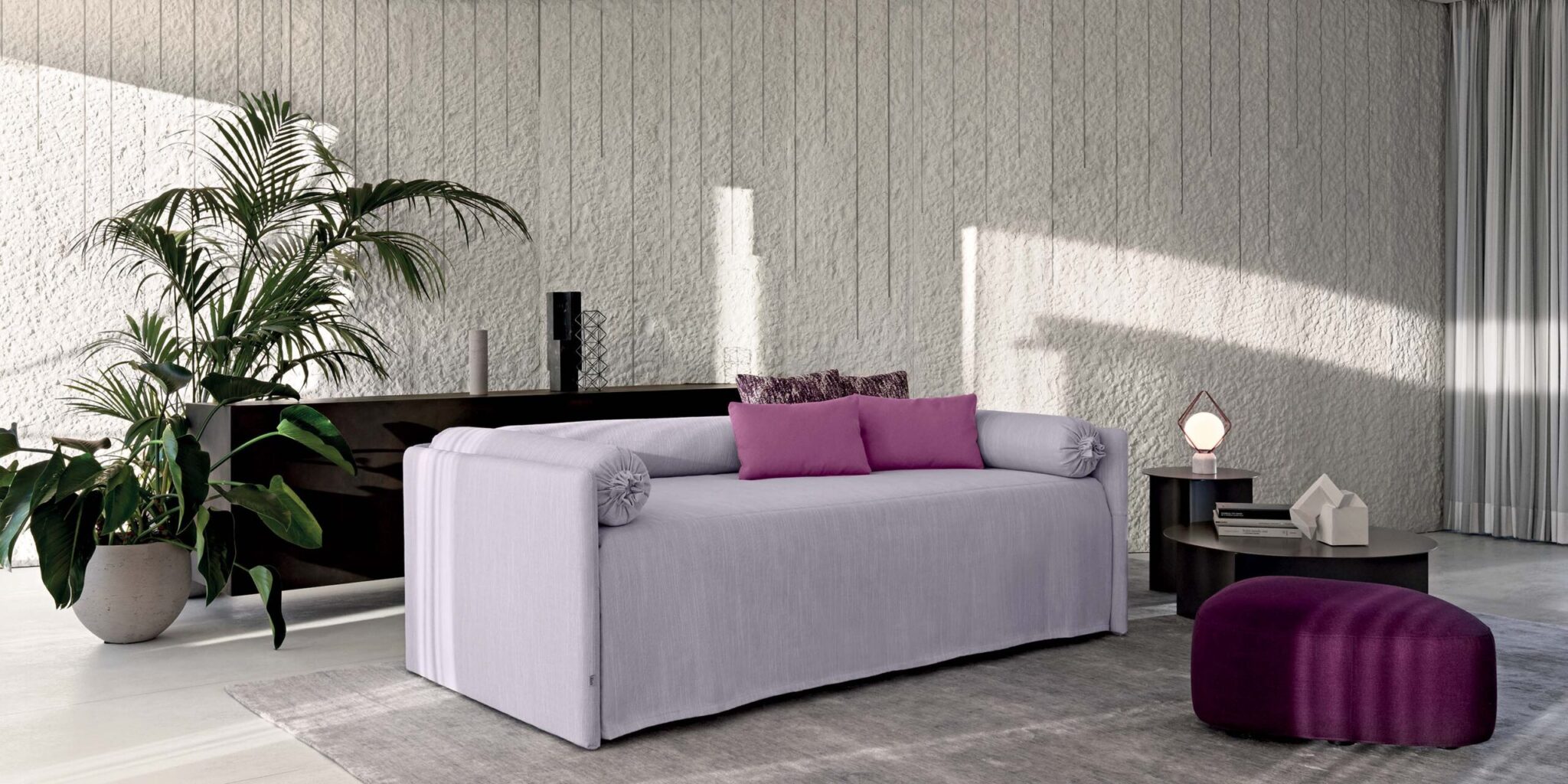 Elegant living room with lavender sofa, magenta cushions, purple ottoman; sculptural Brokis lamp graces sideboard in sunlight.