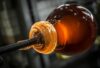 A close-up of molten handblown Brokis glass twirls on a blowpipe, glowing orange and translucent.