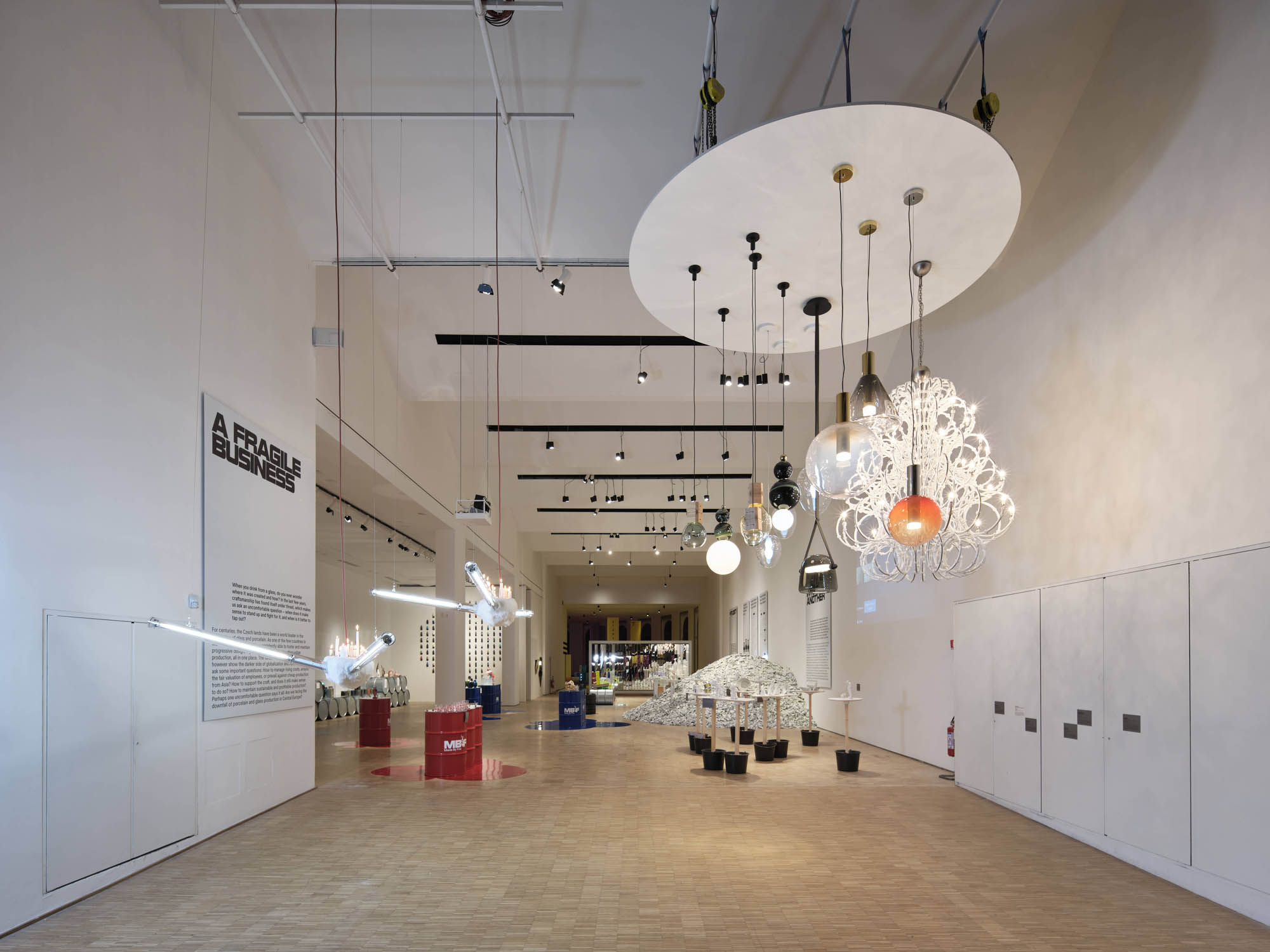 A spacious, modern gallery with soaring ceilings showcases hand-blown, sculptural Brokis lights above a sleek, minimalist space.
