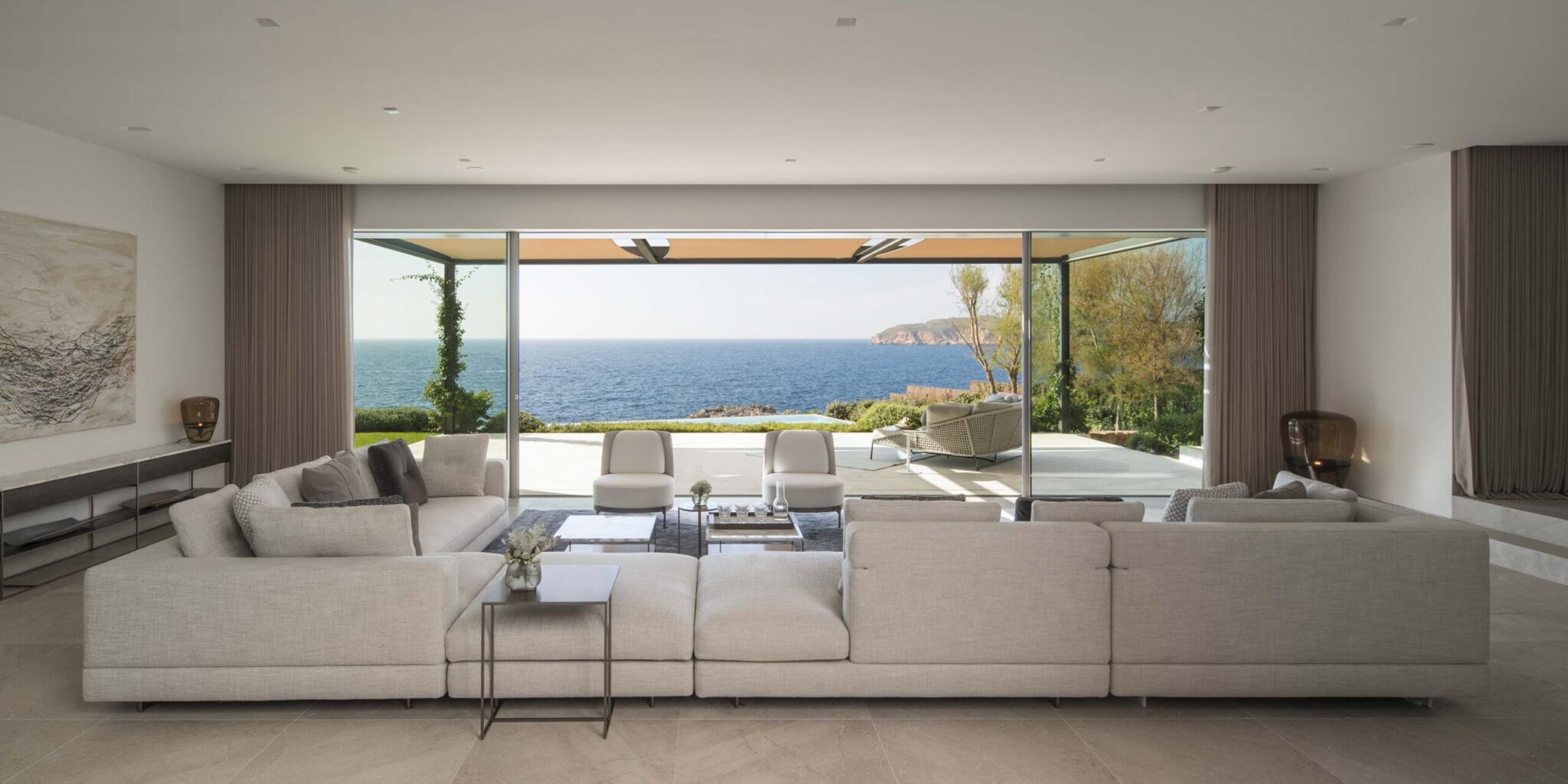A spacious modern living room with a large grey sectional, Brokis Balloons, and neutral décor opens to an ocean-view patio.