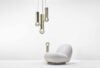 A sculptural white lounge chair on a pristine floor beneath three Brokis Prisma pendants, set against a crisp backdrop.