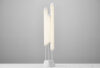 A Brokis Puro floor lamp with three hand-blown, frosted crystal tubes of varying heights glows atop an angular white base.