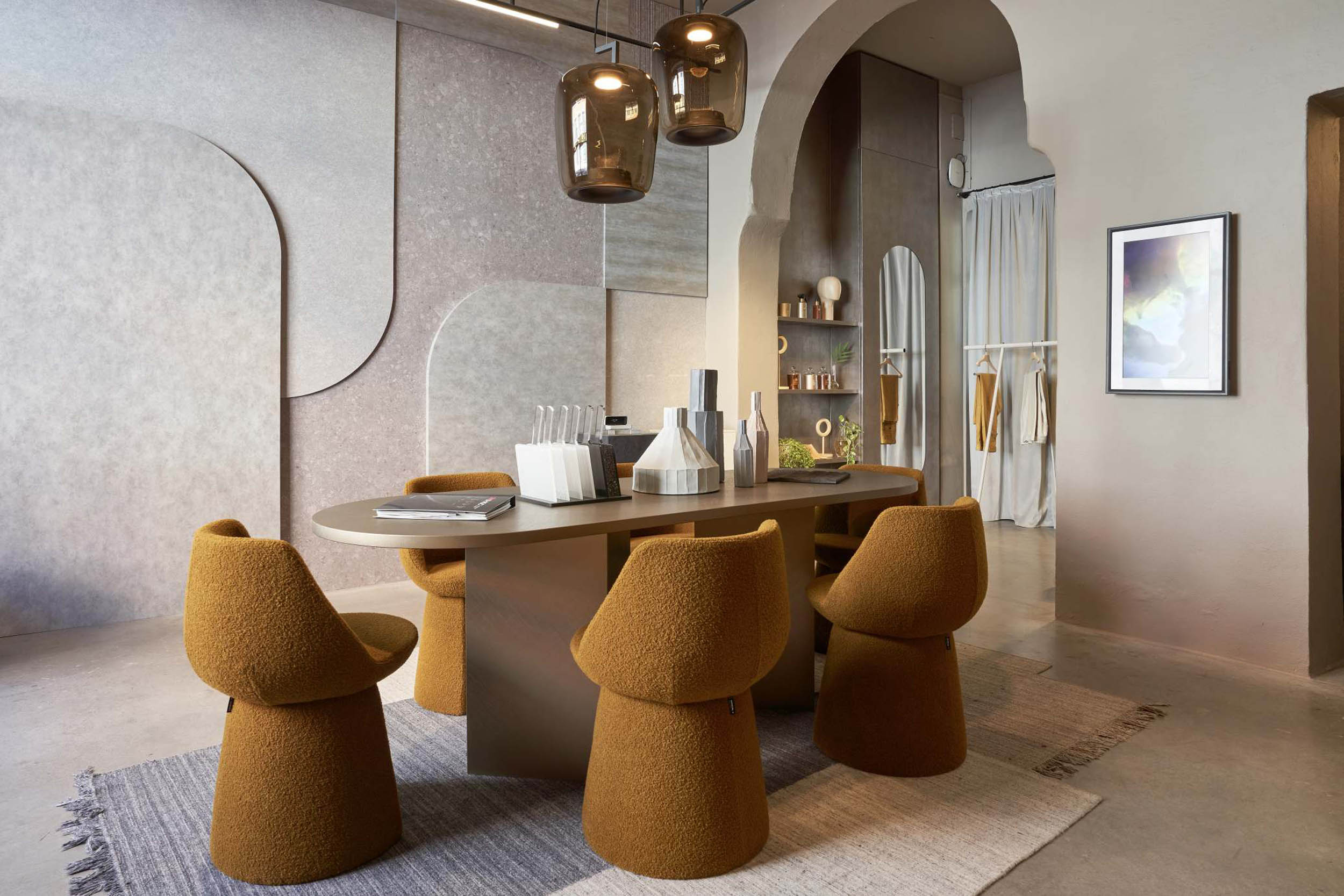 A modern dining room with a sleek oval table, Brokis Double pendants, and curved mustard-yellow chairs on a textured rug.